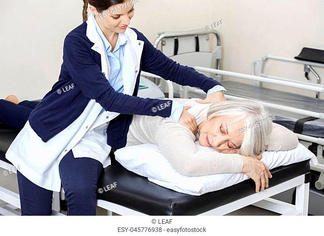 Female physiotherapist giving massage to senior woman in rehab center