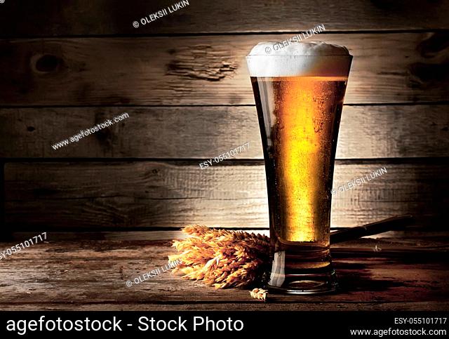 Tall beer glass with beer and ears on wooden background