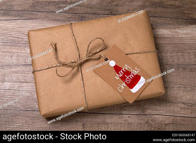 Christmas or New Year gift box wrapped in kraft paper with blank gift tag on old wooden background