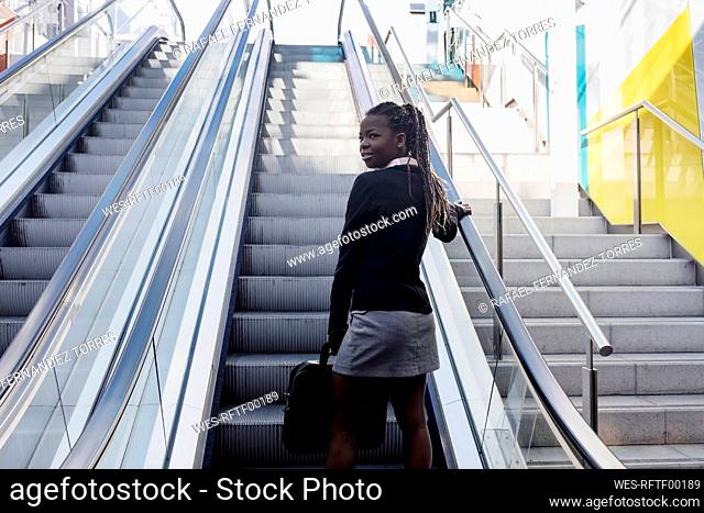 Smiling young woman with laptop bag standing on escalator