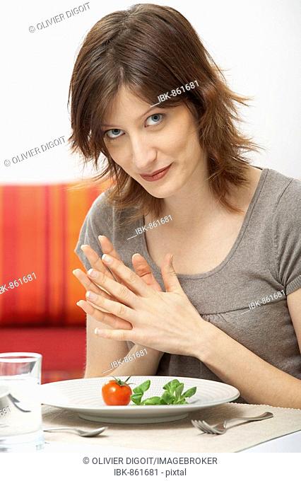 Young woman with a single tomato and piece of lettuce on her plate
