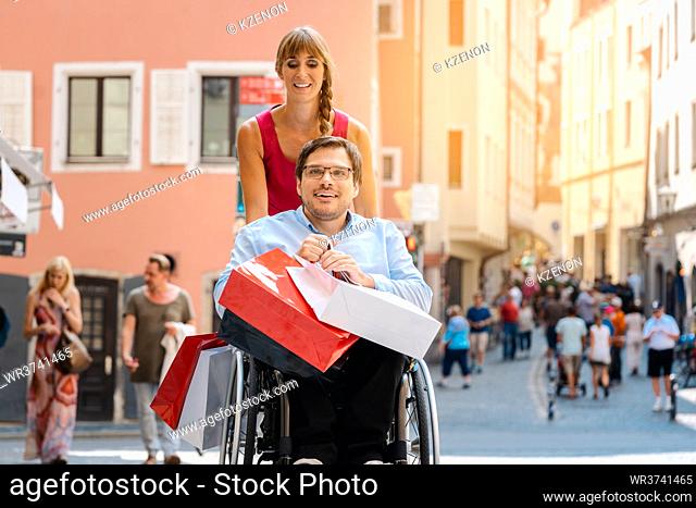 Man in wheelchair being pushed by his friend on a shopping trip with bags