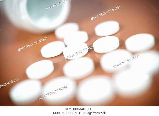 White paracetamol tablets spilling from a bottle against a brown background