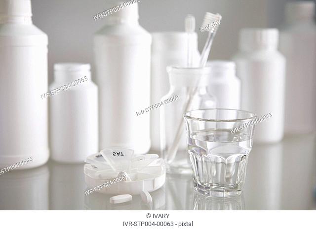 Glass of water with toothbrush in glass jar with pill bottles in the background