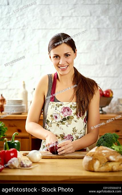 beautiful young woman, brunette cuts onions in the kitchen at a table full of organic vegetables