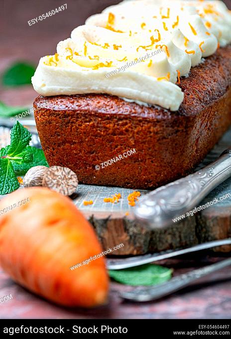 Delicious carrot cake with cottage cheese cream, orange zest and nutmeg on a wooden serving board on a dark background, selective focus