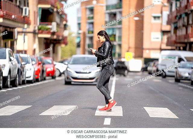 Young woman crossing the pedestrian crossing and using mobile phone