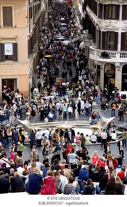 The Via dei Condotti the main shopping street busy with people seen from the Spanish Steps with seated tourists and the Fontana della Barcaccia in the...