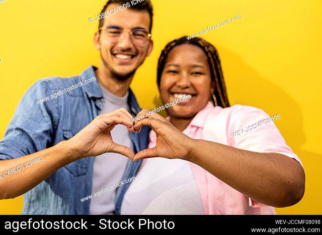 Happy couple gesturing heart shape in front of wall