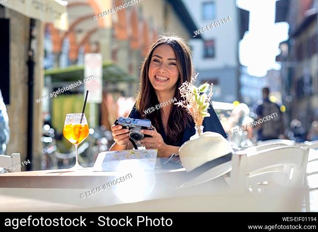 Female tourist with camera smiling at sidewalk cafe on sunny day
