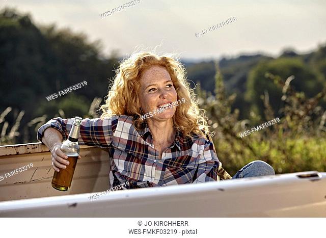 Woman sitting on pick up truck having a beer