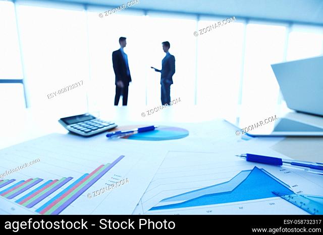 Financial documents , laptop, calculator on table , business team on background