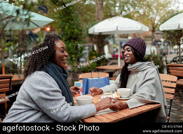 Mother and daughter holding hands and enjoying lunch on cafe patio