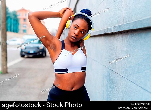 Italy, Milan, Woman in sports clothing and headphones stretching in city