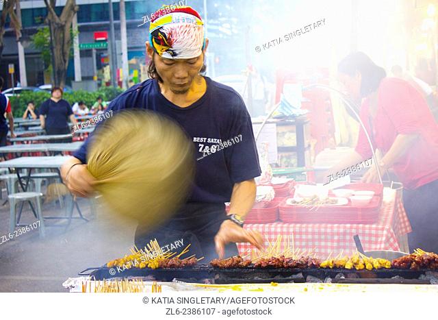 Man cooking Satay and fanning the smoke in Singapore. Satay is street food that locals cannot live without and travelers must have for a true Singapore dining...