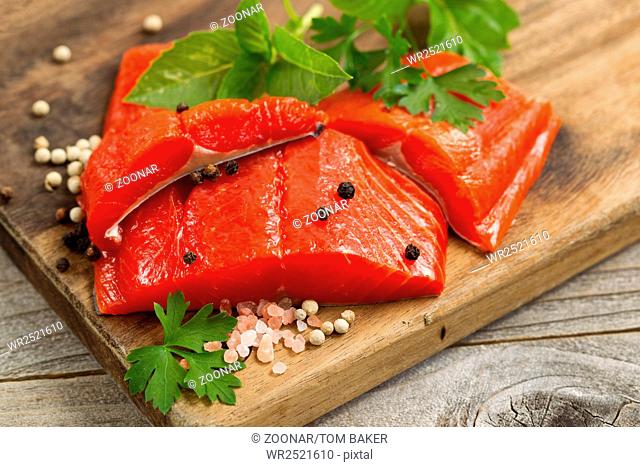 Fresh bright red Copper River Salmon fillets on rustic wooden server with spices and herbs