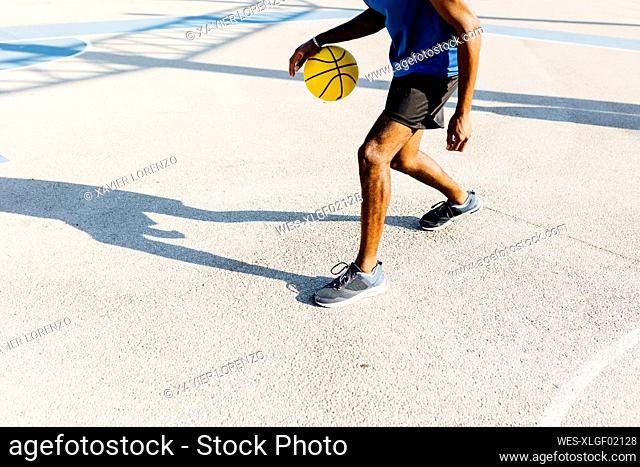 Young man dribbling basketball at sports court during sunny day