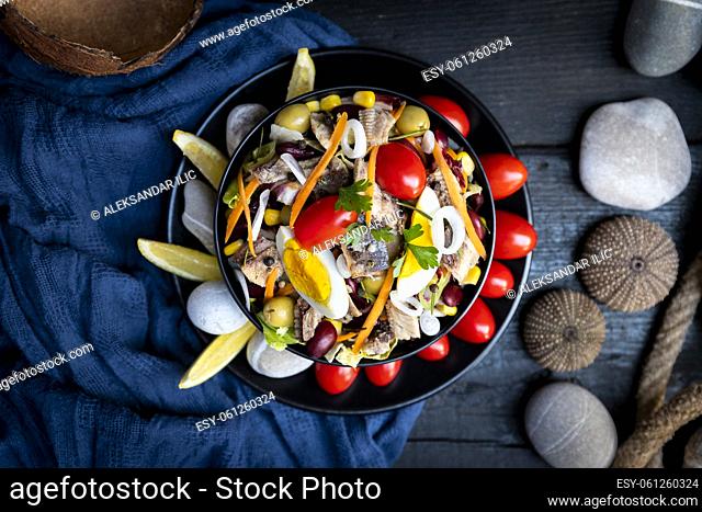Fish salad with sardines, harringe, tuna, tomato, lemon, lettuce, cabbage, olives, beans, corn, carrotes and eggs on rustic kitchen table