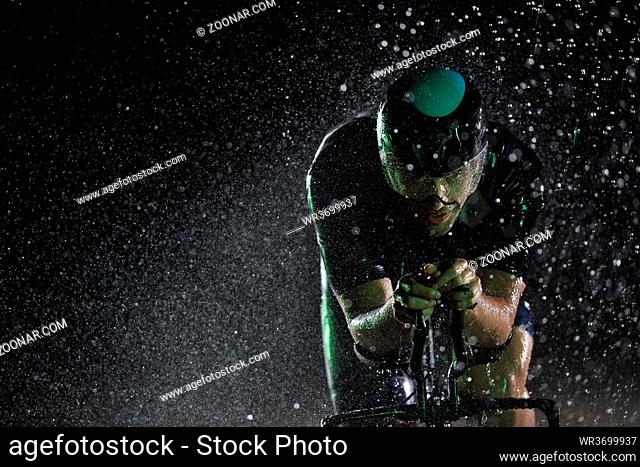 triathlon athlete riding professional racing bike fast at night with bad weather and falling rain