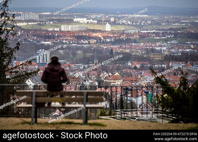 04 February 2023, Baden-Württemberg, Stuttgart: A woman sits on a bench at the Geroksruhe viewpoint in changeable weather and enjoys the view
