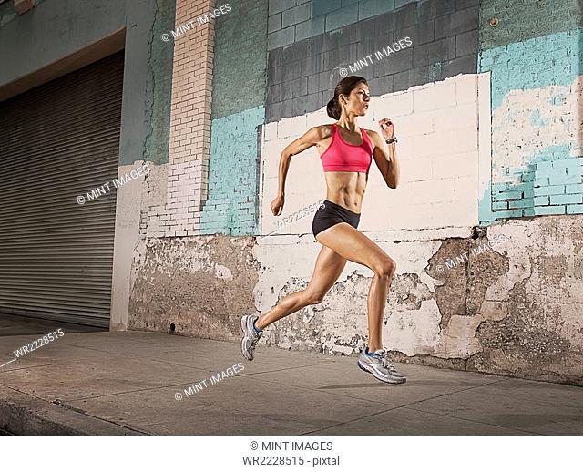 A woman running along an urban street past buildings with peeling paint and a metal shutter