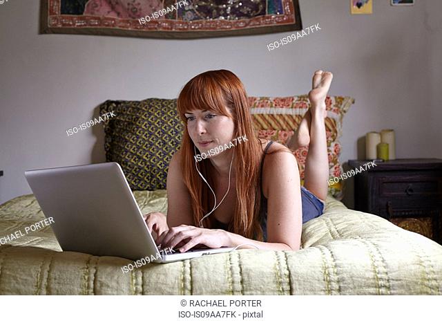 Mid adult woman lying on bed using laptop