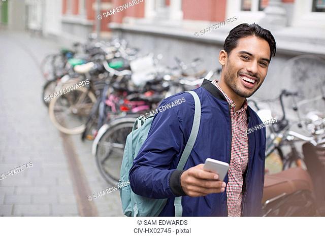 Portrait enthusiastic young man with cell phone at bike rack on city street