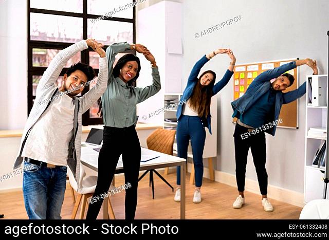 Group Of Happy Young Businesspeople Doing Stretching Exercise In Office