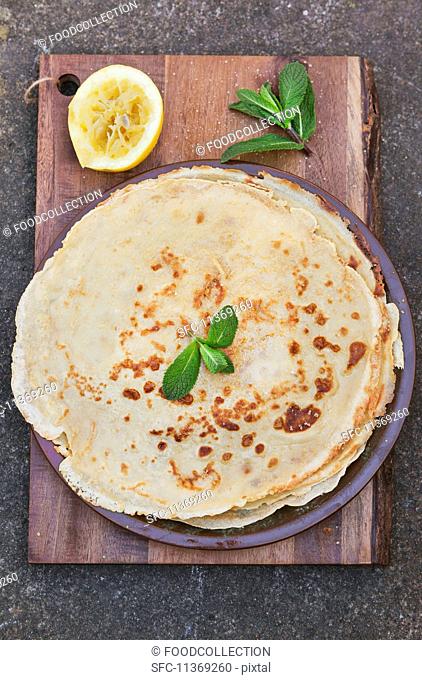A stack of crepes with a juiced lemon and mint