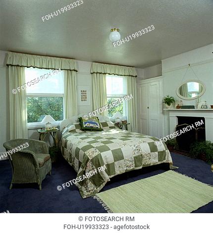 Green+white patchwork quilt on bed in bedroom with Lloyd Loom armchair and blue carpet with green rug