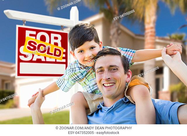 Mixed Race Father and Son Celebrating with a Piggyback in Front Their House and Sold Real Estate Sign