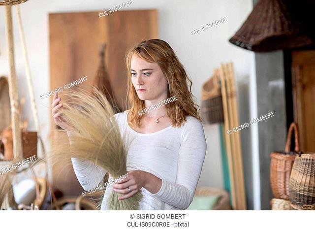 Young female basket maker examining dried grasses in workshop