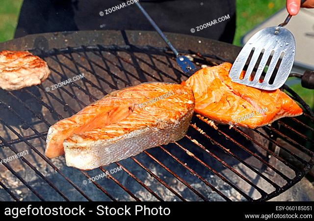 Close up cooking salmon fish steak and fillet on on bbq grill grate, high angle view