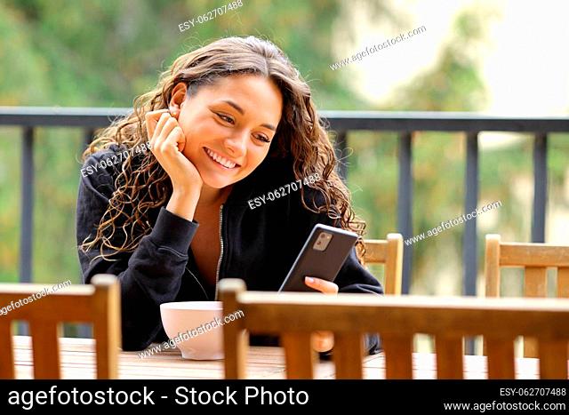 Happy woman in a balcony smiling using smart phone
