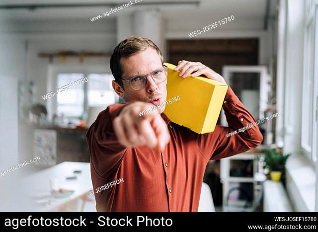 Businessman pointing and holding yellow box in office