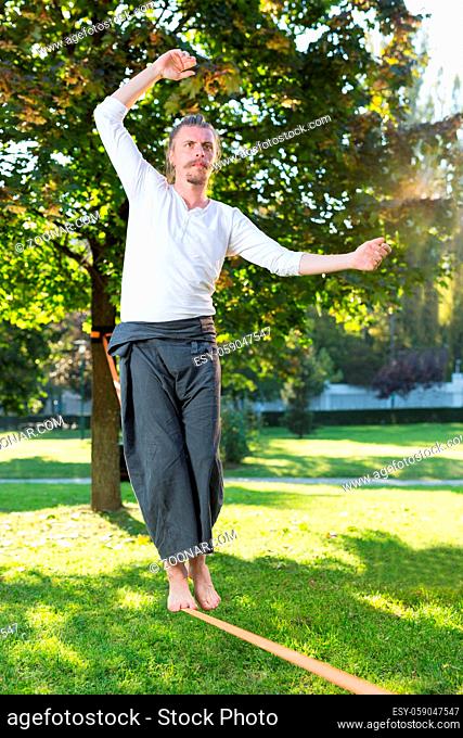 Man walking barefoot on slackline in park with arms out and deep concentrated facial expression