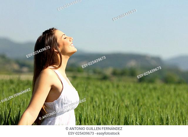 Girl breathing fresh air with white dress in a green wheat meadow