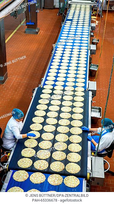 Employees inspect the base used for frozen pizzas at a production line in the pizza plant of food manufacturer Dr. Oetker in Wittenburg, Germany