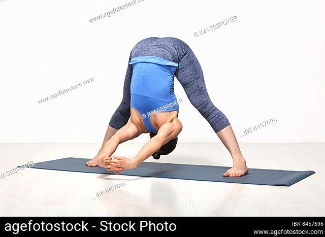 Beautiful sporty fit woman practices Ashtanga Vinyasa yoga asana Prasarita padottanasana C, wide legged forward bend C