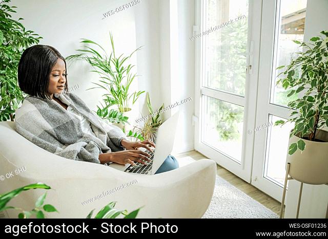 Young businesswoman using laptop sitting in armchair at home