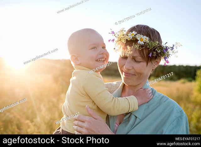 Woman wearing wreath while carrying cheerful son during sunny day