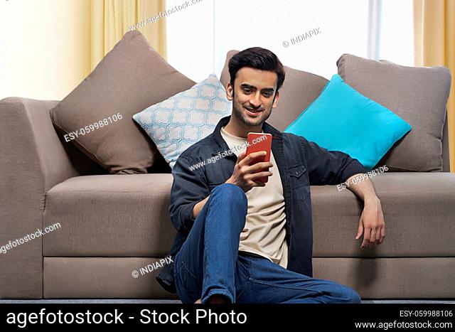 A young man sitting in his living room looking into his mobile