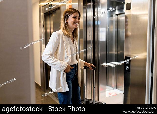 Happy businesswoman with suitcase walking into elevator
