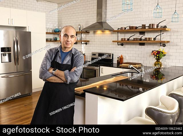 Man leaning against kitchen countertop with arms crossed looking into camera