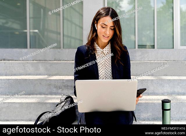 Businesswoman working on laptop while sitting on staircase