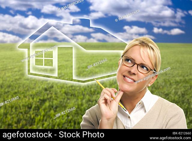 Contemplative woman in grass field looking up and over to the side with ghosted house figure behind