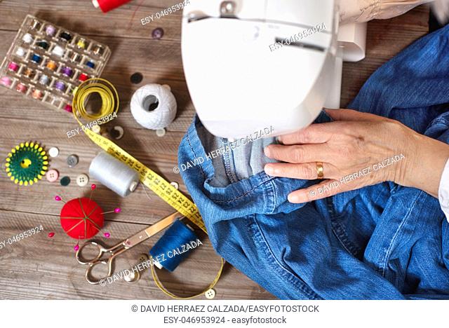 Close-up top view, of senior woman hands seamstress sewing jeans on electrical sewing machine