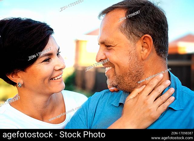 Portrait of a happy married couple in close-up. A man and a woman look at each other and smile sincerely. A middle-aged Caucasian husband and wife on the street...