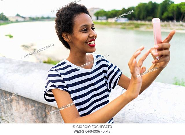 Smiling young woman using cell phone at the riverside