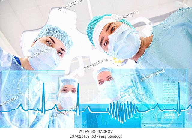 surgery, healthcare, medicine and people concept - group of surgeons in operating room at hospital looking into camera with cardiogram and virtual screen...